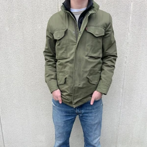 Grön jacka från Levi Strauss & Co - Säljer en snygg grön fieldjacka från Levi Strauss & Co. Jackan har en stilren design med fyra fickor framtill och en hög krage. Perfekt för höst och vår. Hör av er vid frågor!👍
