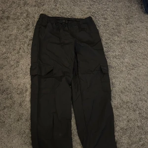 Svarta cargobyxor från Missy Empire - Snygga svarta cargobyxor från Missy Empire med praktiska fickor på sidorna. Byxorna har en loose passform och dragsko i midjan för justerbar komfort. Perfekta för en avslappnad stil.