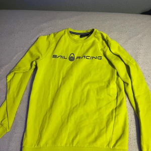 Gul tröja från Sail Racing - Säljer en gul tröja från Sail Racing med långärmad design. Tröjan har en rund halsringning och ett tryck med märkesloggan på framsidan. Perfekt för en sportig look! (Tröjan har en liten svart färgfläck som inte syns så mycket. Därför säljer jag den) storlek 160 barnstorlek.