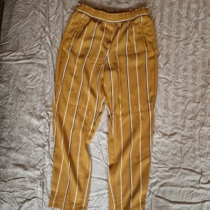 Gulrandiga byxor från H&M - Snygga gulrandiga byxor från H&M med elastisk midja för extra komfort. Byxorna har ett stilrent randigt mönster i vitt och svart som ger en modern look. Perfekta för en avslappnad stil. Liten fläck på framsidan se bild