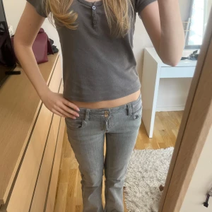 Grå jeans - Snygga grå jeans med låg midja och bootcut-stil. Byxorna har en klassisk design med två knappar och dragkedja framtill. Innerbenslängden är 73cm och midjemåttet är 32cm men passar större då de är väldigt stretchiga!!❤️❤️de har en liten defekt nere vid fötterna men inget som syns se sista bild!🥰