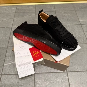 Svarta loubs storlek 43 - Snygga svarta sneakers från Christian Louboutin med ikoniska röda sulor. Skorna har nitar på tån och är tillverkade i mocka med snörning. Perfekta för att ge en edgy touch till din stil.Storlek 43 pris kan diskuteras 