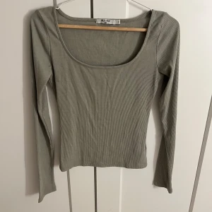 Grön ribbad topp från NA-KD - Säljer en stilren grön ribbad topp från NA-KD. Toppen har en fyrkantig urringning och långa ärmar, perfekt för en chic och enkel look. Passar bra till både jeans och kjol. Perfekt för höst och vår!