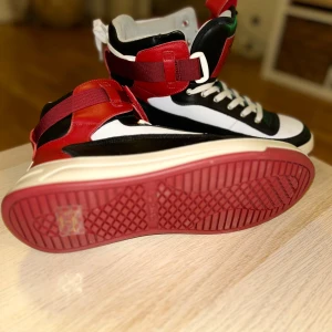 Svartvita sneakers med röda detaljer - Snygga sneakers i svart och vitt med röda detaljer. Skorna har snörning och en cool design med en röd sula. Perfekta för en trendig look.