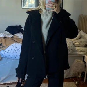 Svart arket kappa - Säljer en stilren svart kappa med knappar framtill. Jackan har långa ärmar och en klassisk krage, perfekt för kyligare dagar. Passar bra till både vardag och mer uppklädda tillfällen. PRIS KAN DISSKUTERAS!!