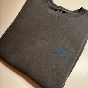 Mads Nørgaard grå sweatshirt - Tidlös grå sweatshirt från Mads Nørgaard. Logotyp i blått på bröstet. Klassisk modell med rund hals. Nyskick.  Nypris: 1099:-