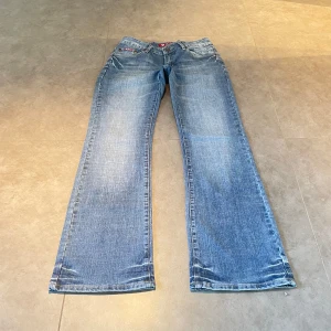 Lågmidjade bootcut jeans med specialfickor - (1) Ljusblåa lågmidjade bootcut jeans med massa fina broderingar på fram och bakfickor och snygg tvätt. Står strlk 31?! men skulle säga strlk 36. Midjemått rakt över: 36cm, innerbenslängd: 81cm❣️
