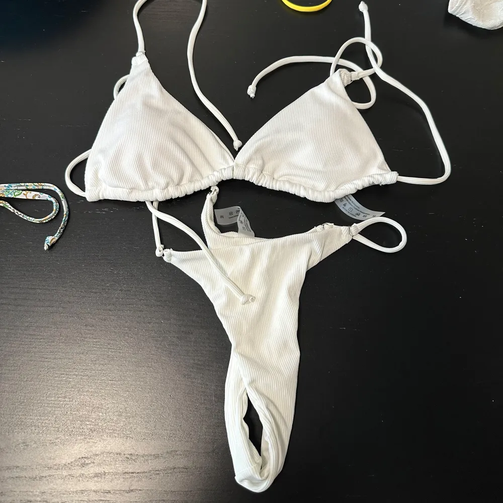 Snygg vit ribbad bikini med knytband. Toppen har justerbara axelband och byxan har en enkel design. Perfekt för soliga dagar på stranden eller vid poolen.. Muu.