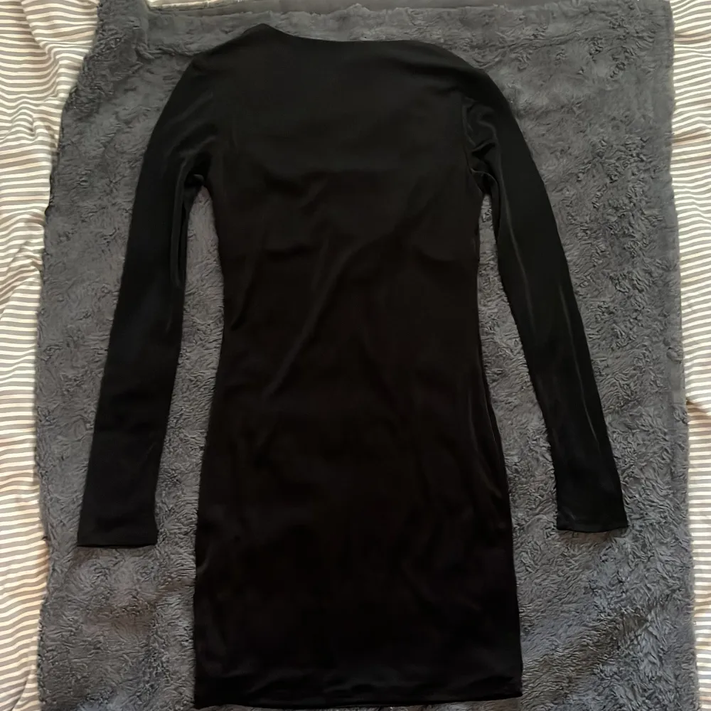 Snygg svart klänning med lång ärm och knytning framtill. Perfekt för en stilren look med en touch av elegans. Klänningen har en åtsittande passform som framhäver figuren.. Mekot.