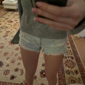 Ljusa jeansshorts med slitningar - Säljer ett par ljusa jeansshorts med coola slitningar och fransiga kanter. Perfekta för en avslappnad stil. De har en klassisk femficksdesign och knappgylf.