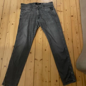 Grå Replay Anbass jeans - Snygga grå Replay Anbass jeans med en klassisk femficksdesign. De har en dragkedja och knapp framtill samt stilrena bakfickor med diskret broderi. Perfekta för en avslappnad look.