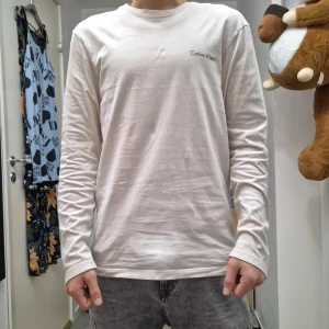 Vit långärmad tröja från Calvin Klein - Säljer en stilren vit långärmad tröja från Calvin Klein. Tröjan har en enkel design med en liten logotyp på bröstet. Perfekt för en avslappnad look. Jag är 176cm lång!