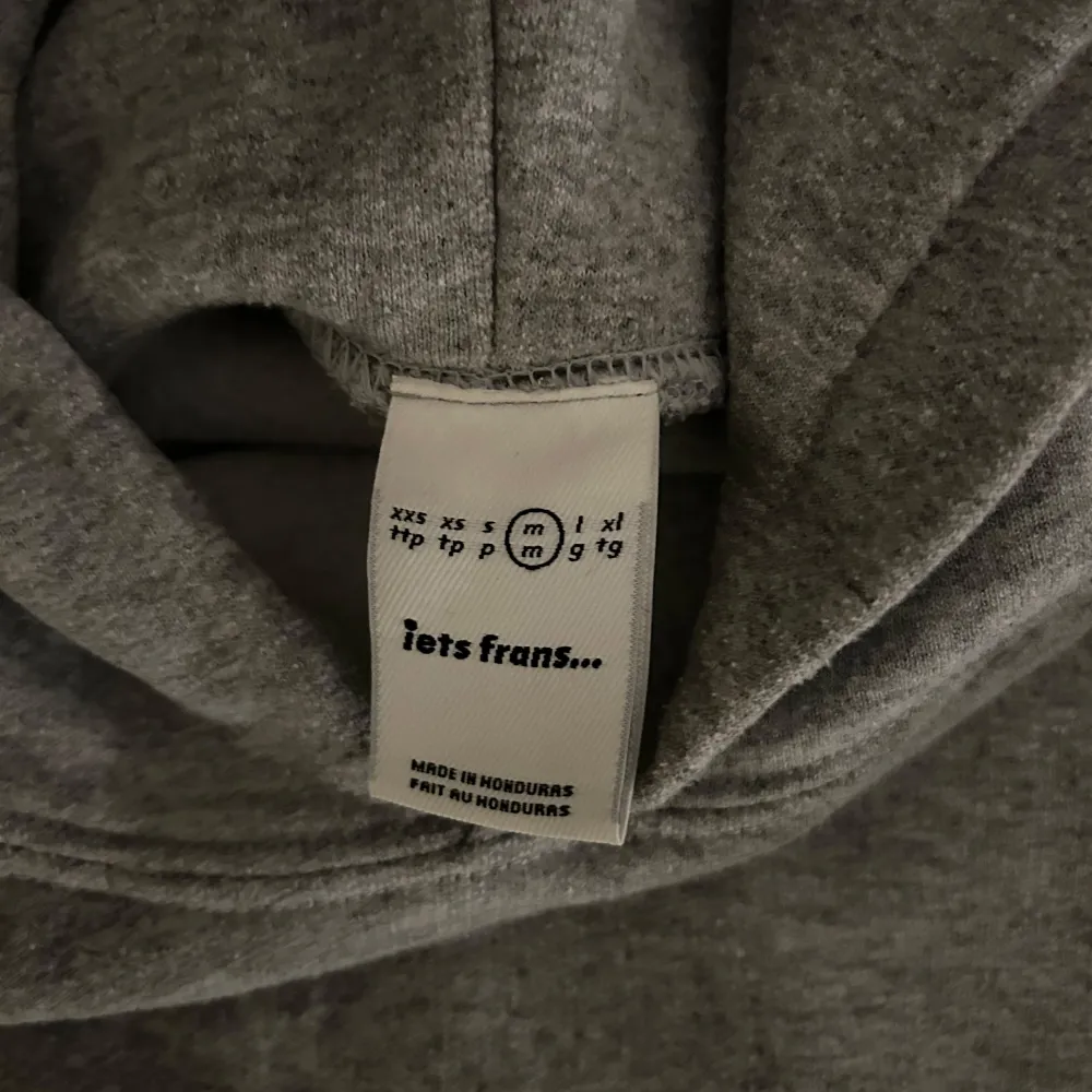 Säljer en stilren grå hoodie från Iets Frans med en praktisk magficka och textdetalj på bröstet. Perfekt för en avslappnad look. 🩶. Neuletakit & Villapaidat.