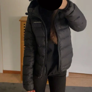 Svart dunjacka från Peak Performance - Säljer en svart dunjacka från Peak Performance. Jackan har en dragkedja framtill och en huva för extra skydd mot kyla. Perfekt för kalla dagar med sin pufferdesign som håller värmen inne.