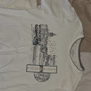 Vit t-shirt med Istanbul-tryck från LC Waikiki - Säljer en vit t-shirt från LC Waikiki med ett coolt Istanbul-tryck. T-shirten har korta ärmar och en rund halsringning med grå kant. Perfekt för en avslappnad stil.