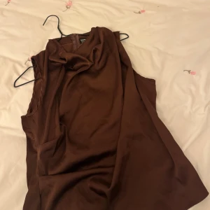 Brun ärmlös topp från Seventy - Snygg brun ärmlös topp från Seventy i ett mjukt och följsamt material. Perfekt för en stilren look. Toppen har en elegant drapering vid halsen som ger en extra touch av stil.