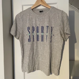 Grå t-shirt från Gina Tricot - Säljer en grå t-shirt från Gina Tricot med texten ”sporty”. T-shirten har en rund halsringning och korta ärmar. S/M