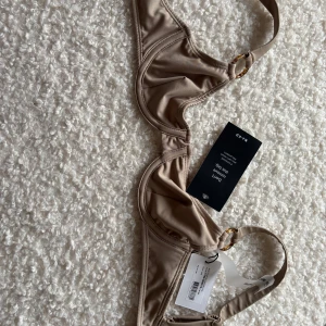 Beige brun bikiniöverdel med ringdetalj - Snygg beige brun bikiniöverdel från baks med stilren design och ringdetalj vid axelbanden. Perfekt för en dag på stranden eller vid poolen. Tillverkad i ett mjukt och bekvämt material. Helt ny, storlek 70B