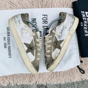 Golden Goose sneakers med stjärndetaljer - Snygga Golden Goose sneakers i vitt med grå stjärndetaljer och handskrivna texter. Skorna har en vintage-look med snörning och en bekväm sula. Perfekta för en avslappnad stil.