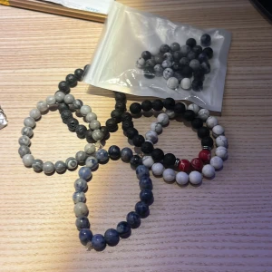Flera pärlarmband i olika färger - Säljer ett set med flera pärlarmband i olika färger. Armbanden har pärlor i svart, grått, blått, vitt och rött. Perfekt för att mixa och matcha till olika outfits.