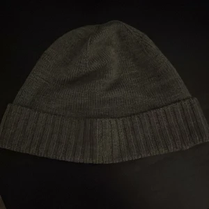 Grå mössa från Polo Ralph Lauren - Snygg grå stickad mössa från Polo Ralph Lauren. Perfekt för kyliga dagar med sin ribbade kant som ger extra värme och stil. En klassisk accessoar för garderoben. Nästan helt nytt skick.