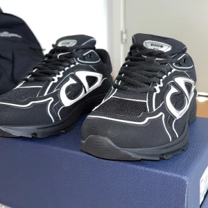 Svarta sneakers från Dior - Snygga svarta sneakers från Dior (B30s)  med vita detaljer och märkets logga på sidan. Skorna har snörning och en modern design som passar perfekt för en stilren look. Dom är helt nya och kommer med boxen och dustbag