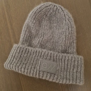Grå stickad mössa från Carin Wester - Snygg grå stickad mössa från Carin Wester med ribbad design och ett diskret CW-märke framtill. Perfekt för kyliga dagar och ger en stilren touch till din outfit.