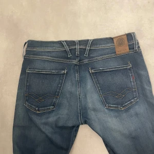 Blå jeans från Replay - Snygga blå jeans från Replay i modellen Anbass. De har en klassisk femficksdesign med diskreta slitningar och en knappgylf. Perfekta för en avslappnad stil. Hör av er om ni har frågor