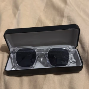 Transparenta solglasögon från All Cap One - Snygga solglasögon med transparent båge och mörka linser från All Cap One. Perfekta för en stilren look. Kommer i ett elegant svart fodral. Det är även lite repor men det är inget man merker.