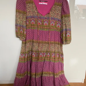 Mönstrad klänning med rosa och gröna detaljer - Säljer en färgglad klänning med ett unikt mönster i rosa, grönt och flerfärgat. Klänningen har en v-ringad hals och trekvartsärmar