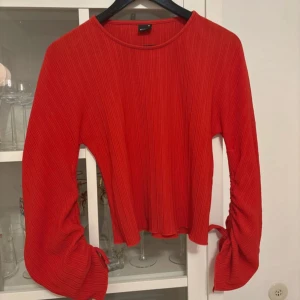Röd ribbad tröja med knyt - Säljer en snygg röd ribbad tröja med långa ärmar och knytning vid ärmsluten. Perfekt för att ge en färgklick till din outfit. Tröjan har en modern och stilren design.