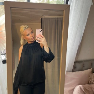 Svart blus med hög krage - Elegant svart blus med hög krage och långa ärmar. Perfekt för en stilren look. Blusen har en lös passform och är tillverkad i ett lätt och luftigt material.