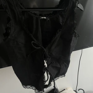 Svart korsettopp från BIKBOK - Snygg svart korsettopp från BIKBOK med spetsdetaljer och knytning framtill. Perfekt för en stilren och edgy look. Toppen har en figurnära passform och är tillverkad i ett mjukt material.