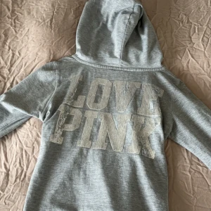 Grå hoodie från VS PINK - Säljer min gråa zip hoodie från Victoria secret PINK med paljettdekorationer på ryggen ”LOVE PINK”. Perfekt skick förutom att det inte finns ett snöre genom luvan men går nog att använda ett eget. Storlek L men passar även M och S! KOMMER INTE SÄLJA DEN BILLIGARE