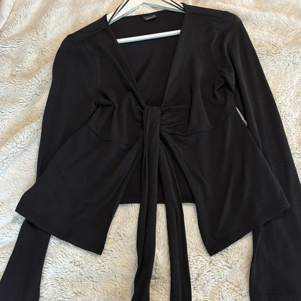 Snygg svart blus med långa ärmar och knytning framtill. Perfekt för en stilren look. Tillverkad i ett mjukt och bekvämt material från Gina tricot. Puserot.