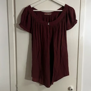 Vinröd blus från Saint Tropez - Säljer en vinröd/lila blus från Saint Tropez med korta ärmar och en lös passform. Blusen har en rund halsringning med två dekorativa knappar framtill. Köpt secondhand, perfekt inför sommaren🌟