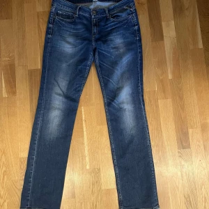 Blå jeans från Replay - Snygga blå jeans från Replay med klassisk femficksdesign och diskreta slitningar. De har en knappgylf och märkesdetaljer på bakfickorna. Perfekta för en avslappnad stil. Storlek 31/31 slim