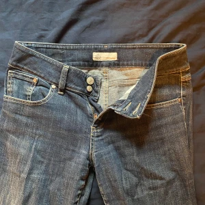 Mörkblå low-waisted jeansbyxor - Snygga mörkblå low waisted jeans med klassisk femficksdesign och knappgylf. De har en lätt tvättad look och raka ben. Perfekta för en avslappnad stil.