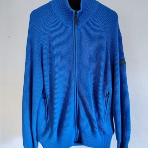 Blå stickad tröja från J.Lindeberg - Säljer en snygg blå stickad tröja från J.Lindeberg. Tröjan har en dragkedja framtill och långa ärmar. Perfekt för kyligare dagar med sin ribbade design och stilrena look. Passar både till vardags och mer uppklädda tillfällen. Mkt fin! 