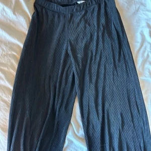 Svarta ribbade byxor använda - Snygga svarta ribbade byxor med elastisk midja. Perfekta för en avslappnad stil med en touch av elegans. De har en loose passform som ger en bekväm känsla hela dagen. Säljs i befintligt skick.