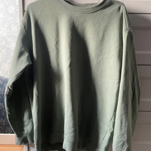 Grön sweatshirt - Säljer en stilren grön sweatshirt med rund halsringning. Tröjan har långa ärmar och ribbade muddar vid ärmslut och nederkant. Perfekt för en avslappnad stil.
