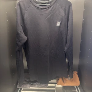 Svart långärmad tröja från Sail Racing - Säljer en stilren svart långärmad tröja från Sail Racing. Tröjan har en rund halsringning och ett diskret märke på bröstet. Perfekt för en avslappnad och sportig look. Släppt lite vid loggan.