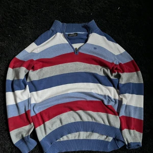 Randig tröja från Hampton Republic - Säljer en randig tröja från Hampton Republic i blått, rött, grått och vitt. Tröjan har en dragkedja vid halsen och ribbade muddar. Perfekt för en avslappnad stil.