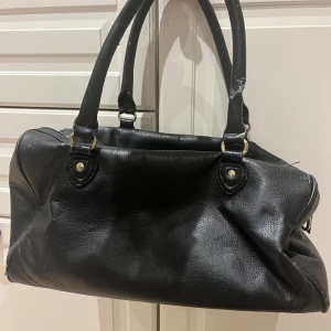 Svart handväska från H&M - Snygg svart handväska från H&M i syntetmaterial. Väskan har två rejäla handtag och en dragkedja upptill för säker förvaring. Perfekt för att bära med sig det nödvändigaste med stil.