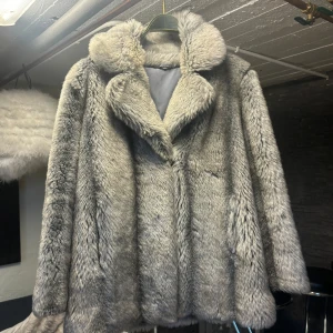 Grå pälsjacka - Säljer en lyxig och varm grå pälsjacka med en elegant krage. Jackan har långa ärmar och en mjuk, fluffig textur som ger en exklusiv känsla. Perfekt för kalla dagar när du vill hålla stilen.