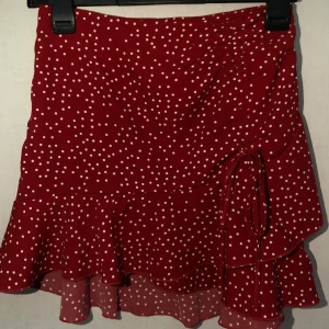 Röd prickig kjol med volang - ❗️TAR ENDAST EMOT SWISH, skriv t mig vid köp ❗️Charmig röd kortkjol med vita prickar och volangdetaljer. Kjolen har en söt knytning på sidan som ger en extra touch. Använd några gånger ❤️