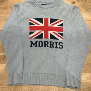 Grå tröja från Morris - Säljer en stilren grå tröja från Morris med Union Jack-motiv och texten 'Morris' på framsidan. Perfekt för en klassisk look.