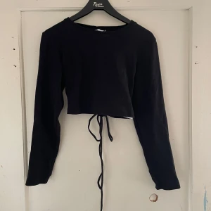 Svart långärmad topp från FB Sister - Säljer en svart långärmad topp från FB Sister i storlek L. Den är croppad och har en snygg snörning i ryggen som ger en cool detalj. Perfekt för både vardag och fest!