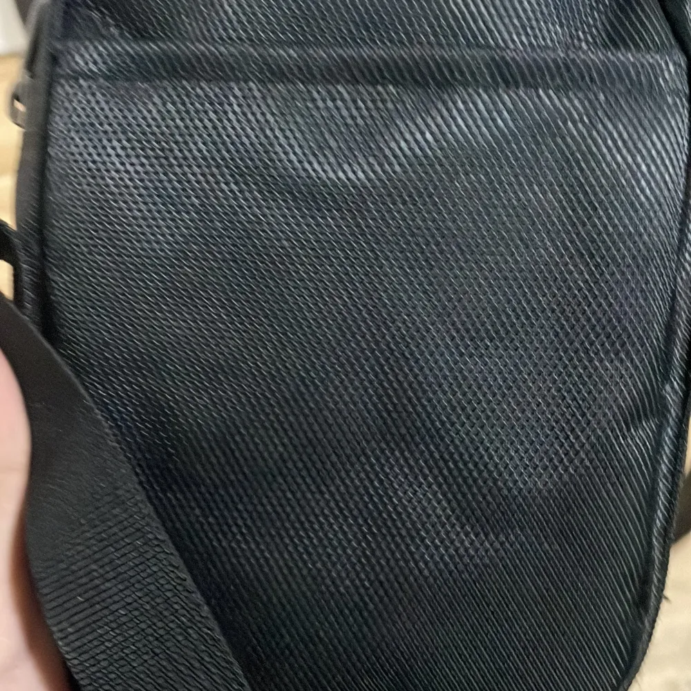 Säljer en snygg och praktisk svart axelväska från Nike. Väskan har ett stort vitt Nike-logotyptryck på framsidan och är tillverkad i slitstarkt syntetmaterial. Perfekt för vardagsbruk eller när du är på språng. Den har en justerbar axelrem och en dragkedja för säker förvaring. Insidan är fodrad i en mörkröd nyans.. Laukut & Käsilaukut.