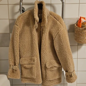 Beige teddyjacka från Missguided - Beige teddyjacka / sherpajacka från Missguided. Jackan har långa ärmar och fickor framtill. Den stängs med drsgkedjs och har en krage som går att knäppa igen.  Stpr i storlek så passar även strlk 36.